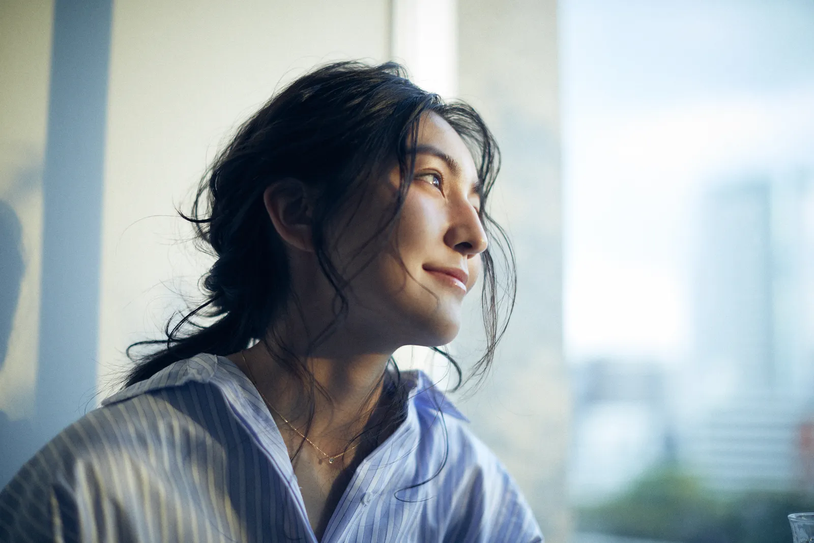 窓辺の光の中で外を見る、ウェーブヘアの女性｜THE BALCONY のスタイル